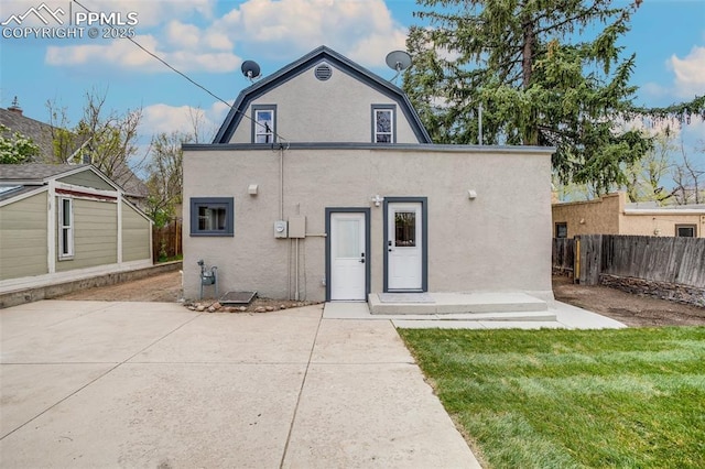 back of house with fence, a gambrel roof, a lawn, stucco siding, and a patio area