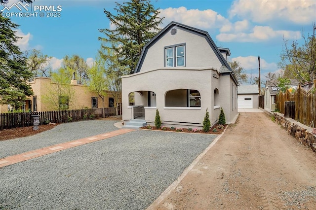 view of front of home with driveway, a gambrel roof, fence private yard, an outdoor structure, and stucco siding