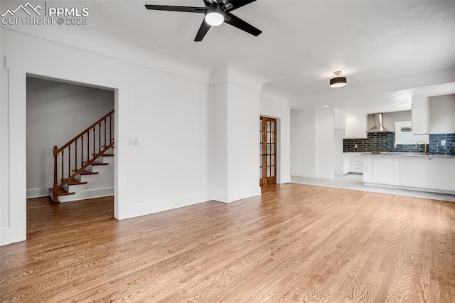 unfurnished living room featuring light wood-style floors, ceiling fan, baseboards, and stairs