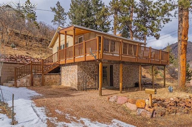 snow covered property featuring a deck, stone siding, and stairs