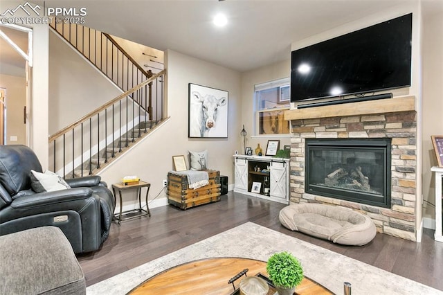 living room with dark wood-style flooring, a stone fireplace, baseboards, and stairs