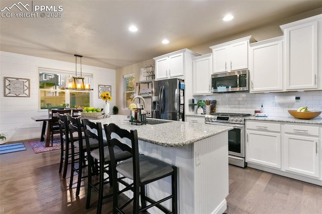 kitchen with appliances with stainless steel finishes, pendant lighting, white cabinets, and a center island with sink