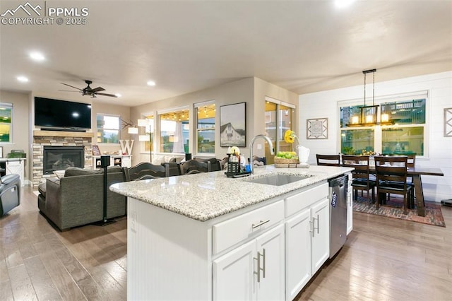 kitchen featuring hanging light fixtures, open floor plan, a kitchen island with sink, a sink, and white cabinetry