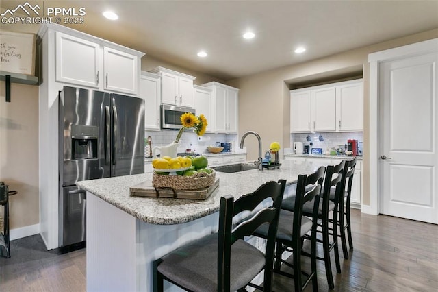 kitchen featuring white cabinets, a breakfast bar area, a kitchen island with sink, stainless steel appliances, and a sink