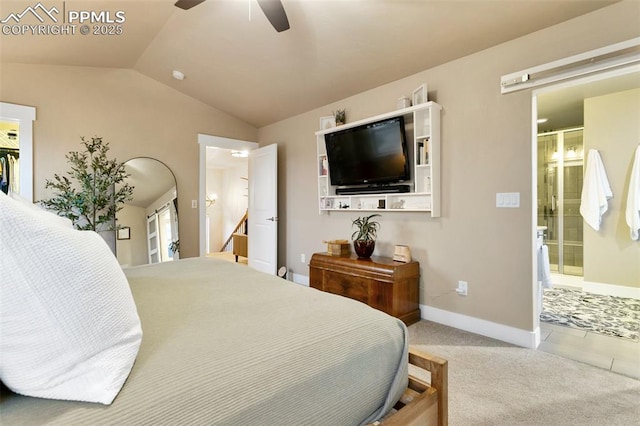 carpeted bedroom featuring a walk in closet, lofted ceiling, ensuite bathroom, a ceiling fan, and baseboards