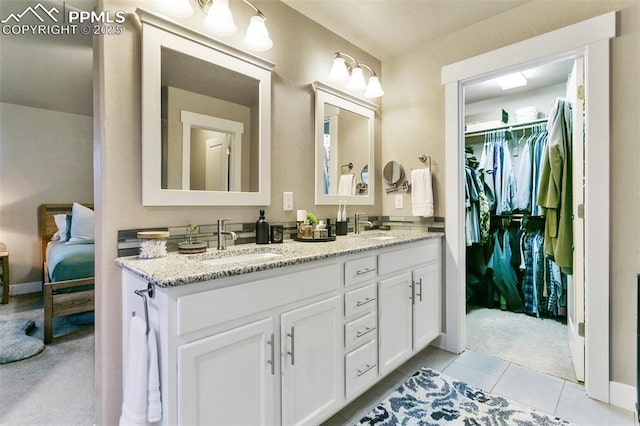 ensuite bathroom featuring tile patterned floors, a sink, a spacious closet, and double vanity