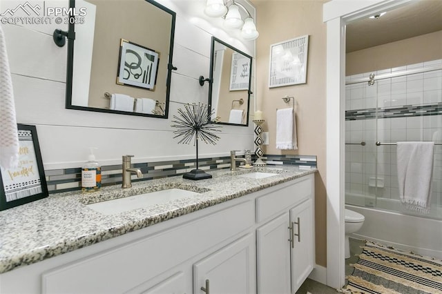 full bath featuring bath / shower combo with glass door, double vanity, a sink, and toilet