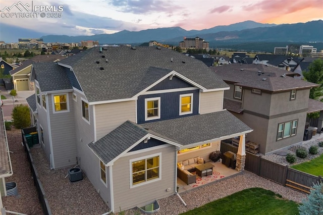 back of house at dusk with a shingled roof, a fenced backyard, an outdoor hangout area, cooling unit, and a mountain view