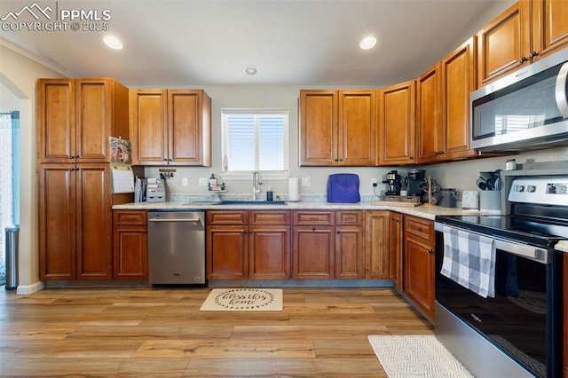 kitchen with light wood-style flooring, recessed lighting, a sink, appliances with stainless steel finishes, and brown cabinetry