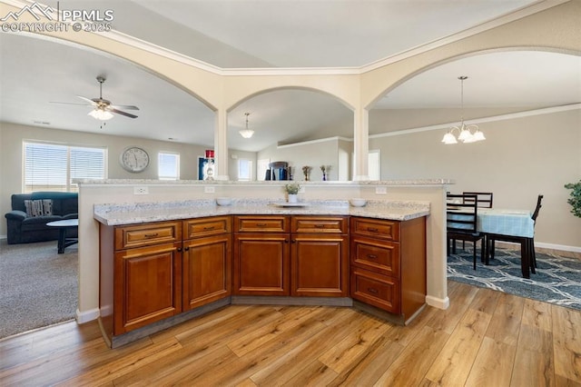 kitchen featuring open floor plan, hanging light fixtures, light wood-type flooring, brown cabinets, and light stone countertops