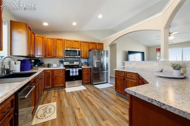 kitchen featuring lofted ceiling, light wood-style flooring, a sink, appliances with stainless steel finishes, and brown cabinetry