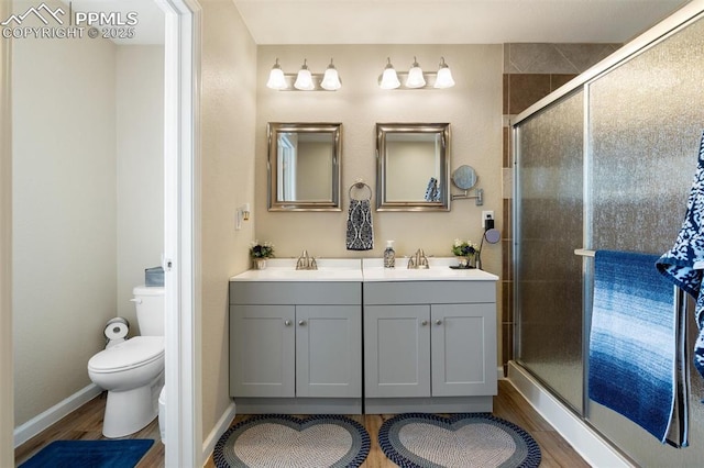 bathroom featuring a sink, a shower stall, toilet, and wood finished floors