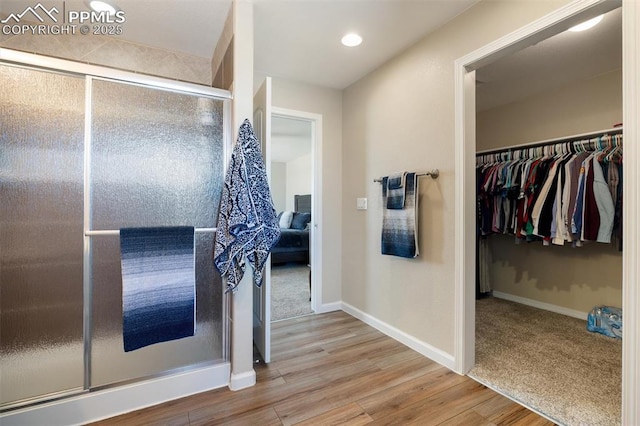 bathroom with recessed lighting, a spacious closet, a stall shower, wood finished floors, and baseboards