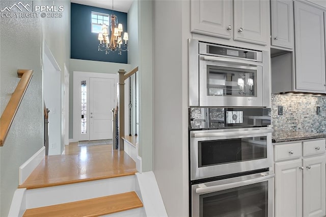 kitchen with tasteful backsplash, double oven, pendant lighting, and a notable chandelier