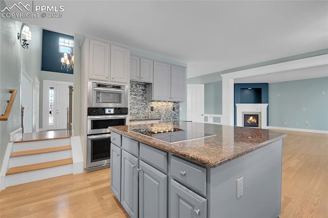 kitchen featuring a kitchen island, black electric stovetop, gray cabinetry, light wood-type flooring, and backsplash