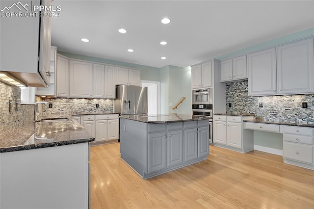 kitchen featuring light wood finished floors, a kitchen island, a sink, dark stone countertops, and stainless steel fridge