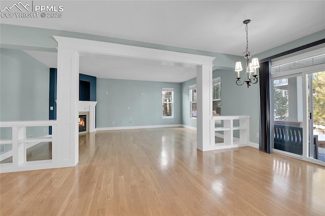 unfurnished dining area with a glass covered fireplace, a notable chandelier, light wood-style flooring, and baseboards