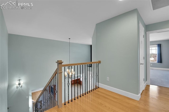 corridor featuring baseboards, visible vents, wood finished floors, an upstairs landing, and a chandelier