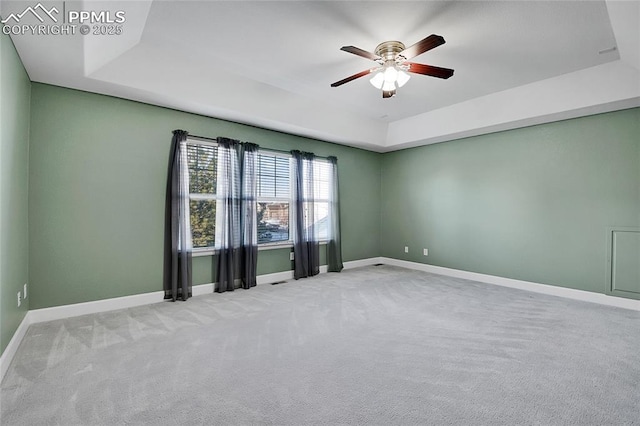 unfurnished room with a ceiling fan, a tray ceiling, light colored carpet, and baseboards