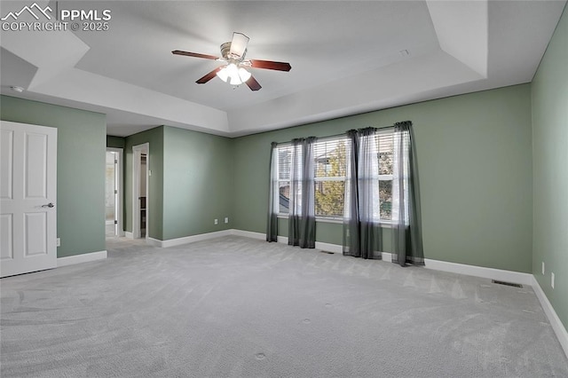 spare room with a tray ceiling, light carpet, ceiling fan, and baseboards