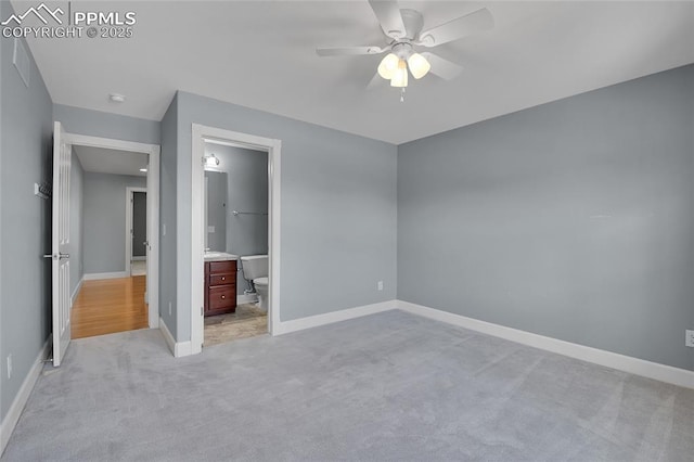 unfurnished bedroom featuring light carpet, ensuite bath, baseboards, and a ceiling fan