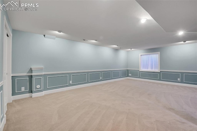 spare room featuring a wainscoted wall, a decorative wall, visible vents, and light colored carpet