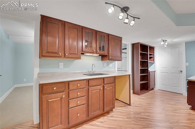 kitchen featuring brown cabinetry, glass insert cabinets, light countertops, light wood-style floors, and a sink