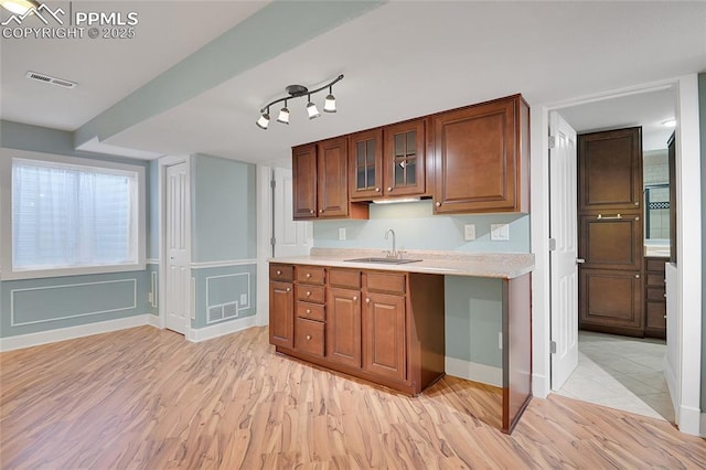 kitchen featuring visible vents, brown cabinetry, glass insert cabinets, light countertops, and a sink