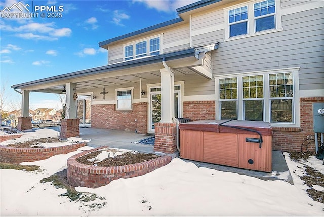 snow covered patio with covered porch and a hot tub