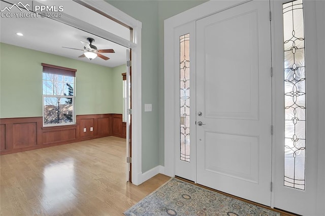 entryway with light wood finished floors, wainscoting, and a ceiling fan