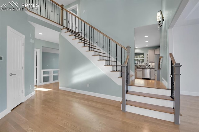 stairway with a towering ceiling, baseboards, and wood finished floors