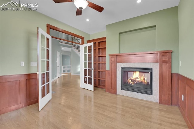 unfurnished living room featuring light wood-style flooring, recessed lighting, a fireplace, french doors, and wainscoting