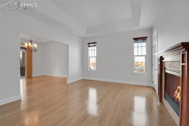 unfurnished living room with light wood-style floors, a glass covered fireplace, a raised ceiling, and plenty of natural light