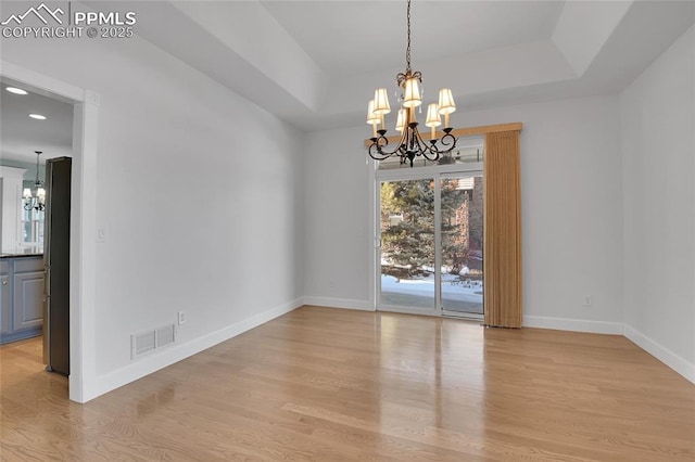 unfurnished dining area featuring baseboards, visible vents, light wood-style flooring, a tray ceiling, and a notable chandelier