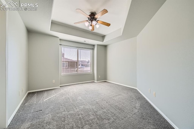 empty room featuring ceiling fan, baseboards, a raised ceiling, and carpet flooring