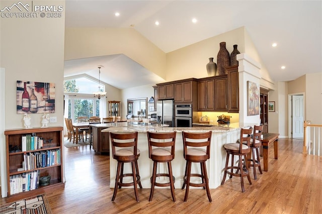 kitchen featuring a breakfast bar area, stainless steel appliances, a peninsula, light wood-type flooring, and light stone countertops