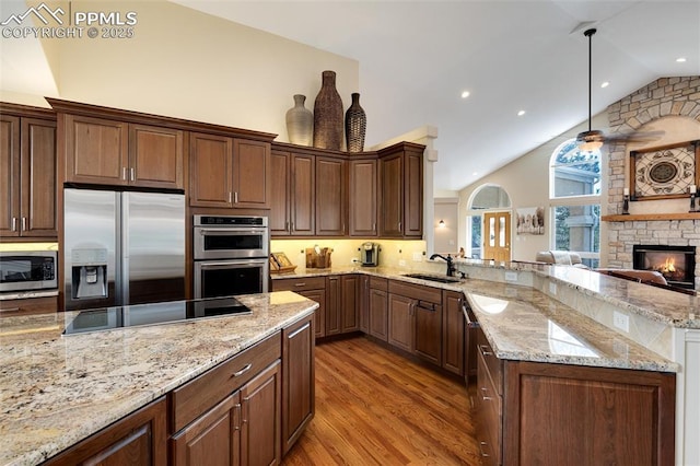 kitchen featuring light stone counters, light wood-style flooring, appliances with stainless steel finishes, a sink, and a peninsula