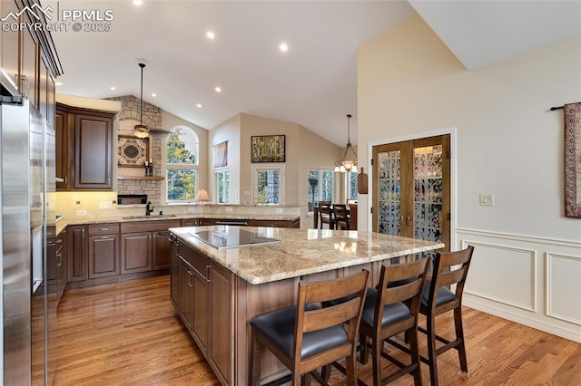 kitchen with black electric stovetop, lofted ceiling, wainscoting, a sink, and light wood-type flooring