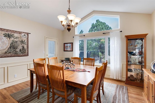 dining area featuring a chandelier, a decorative wall, a wainscoted wall, vaulted ceiling, and light wood finished floors