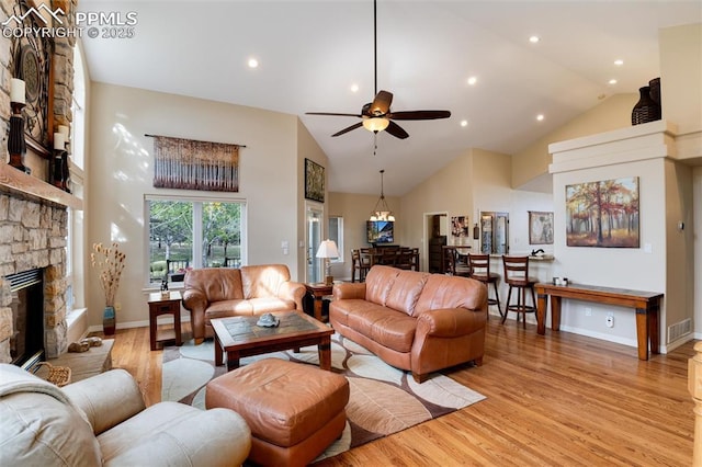 living area featuring visible vents, ceiling fan, a stone fireplace, light wood-type flooring, and high vaulted ceiling