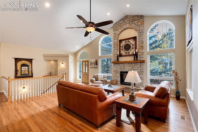 living area featuring baseboards, visible vents, wood finished floors, a stone fireplace, and high vaulted ceiling