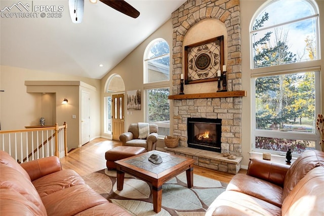 living area featuring high vaulted ceiling, a stone fireplace, wood finished floors, and a wealth of natural light