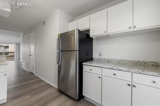 kitchen with light wood-style flooring, visible vents, white cabinets, light countertops, and freestanding refrigerator