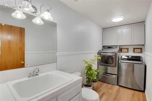 bathroom with wainscoting, a sink, washer and clothes dryer, and toilet