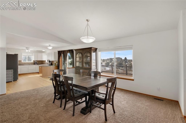 dining space featuring light colored carpet, lofted ceiling, visible vents, and baseboards