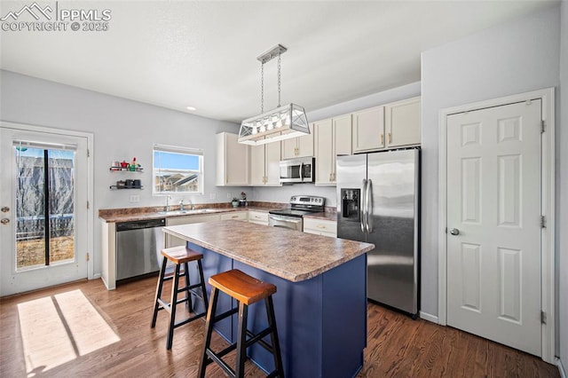 kitchen with dark wood finished floors, appliances with stainless steel finishes, a kitchen breakfast bar, a center island, and a sink