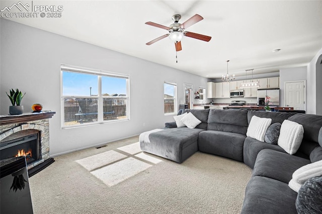 living room with light colored carpet, a stone fireplace, baseboards, and ceiling fan with notable chandelier