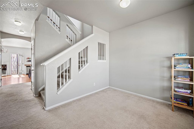 stairway featuring carpet floors, arched walkways, a textured ceiling, and baseboards