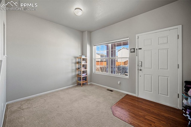 foyer with carpet floors, visible vents, and baseboards