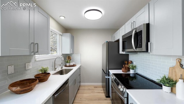 kitchen featuring light wood finished floors, decorative backsplash, stainless steel appliances, light countertops, and a sink